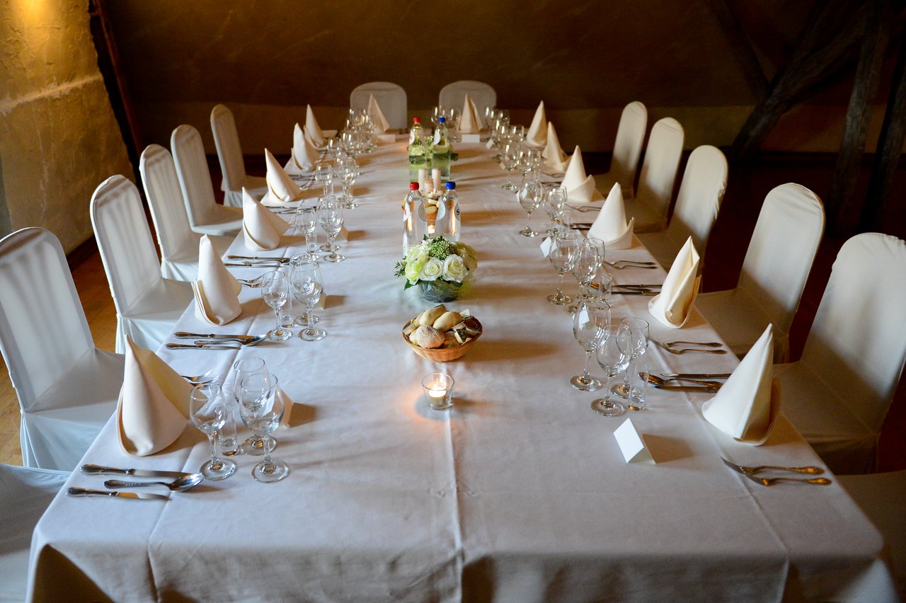 A long wedding reception table set with white tablecloth, folded napkins, glassware, and a floral centerpiece.