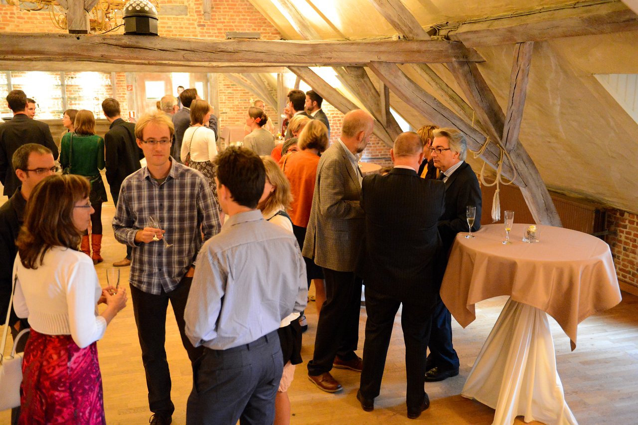 Guests at a wedding reception stand in small groups, chatting and holding drinks in a warmly lit venue.