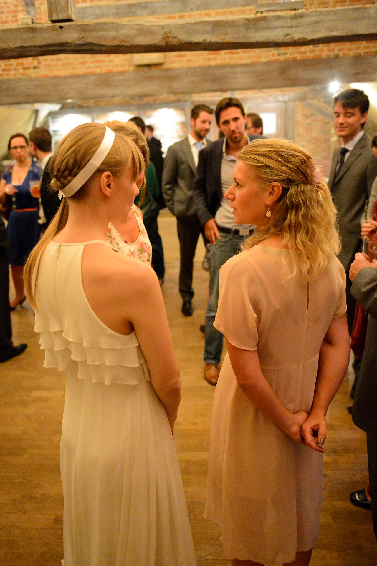 A bride in a white dress talks with a guest in a pink dress at a wedding reception.