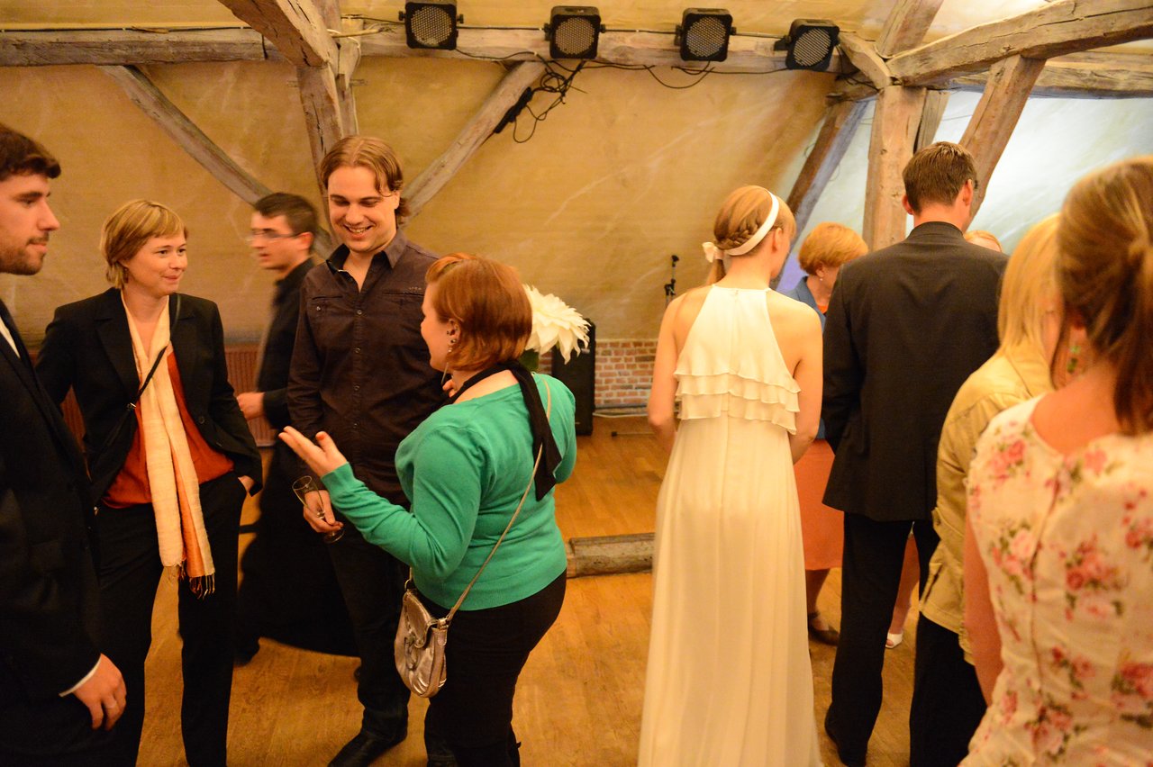 Wedding guests socializing indoors, with a bride in a white dress among the crowd.