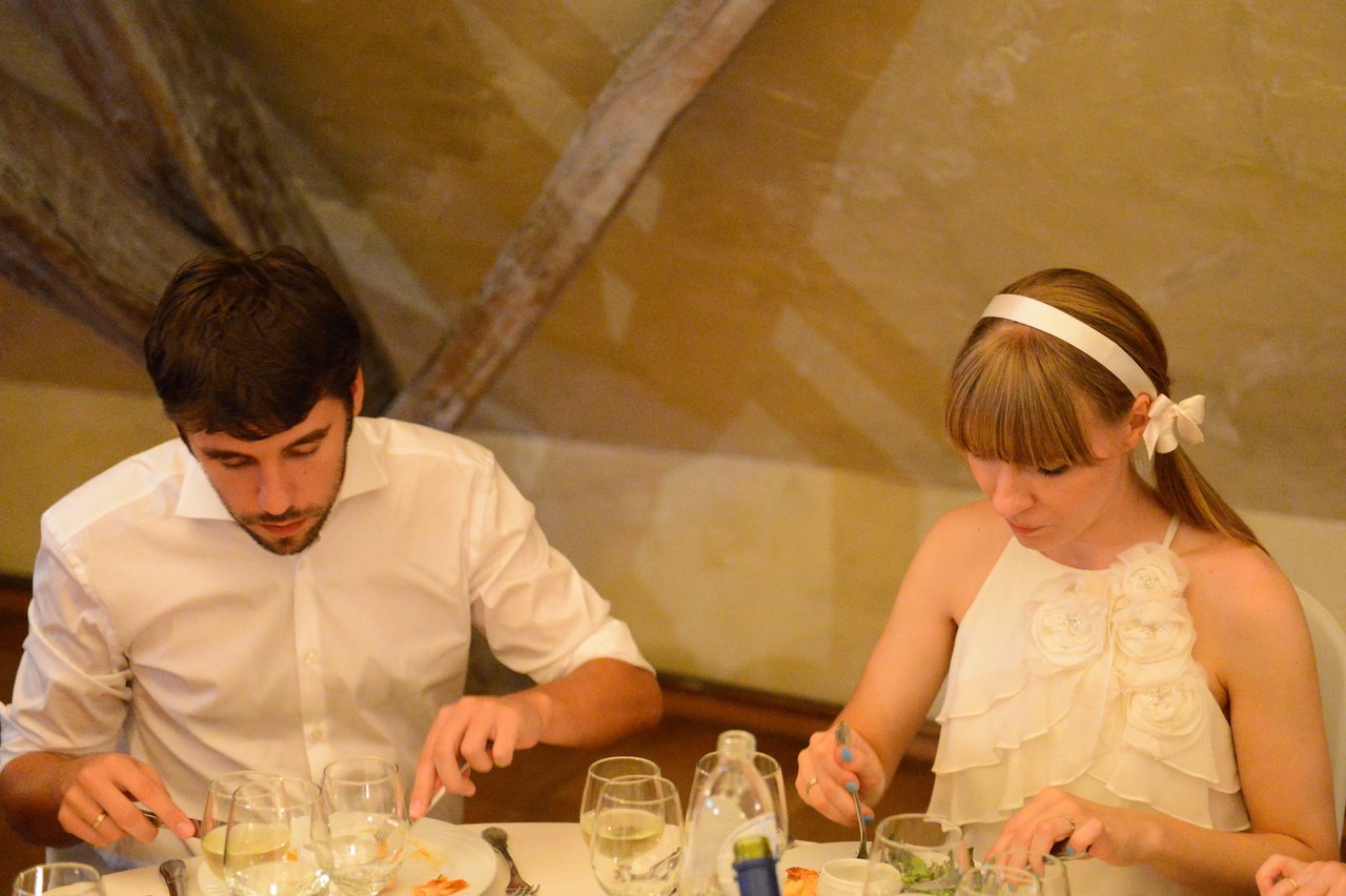 A man and a woman in wedding attire sit at a table, eating their meal during a wedding reception.