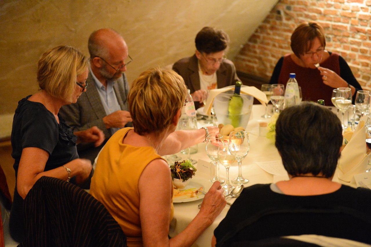 Guests sit around a table at a wedding reception, eating, drinking, and talking.