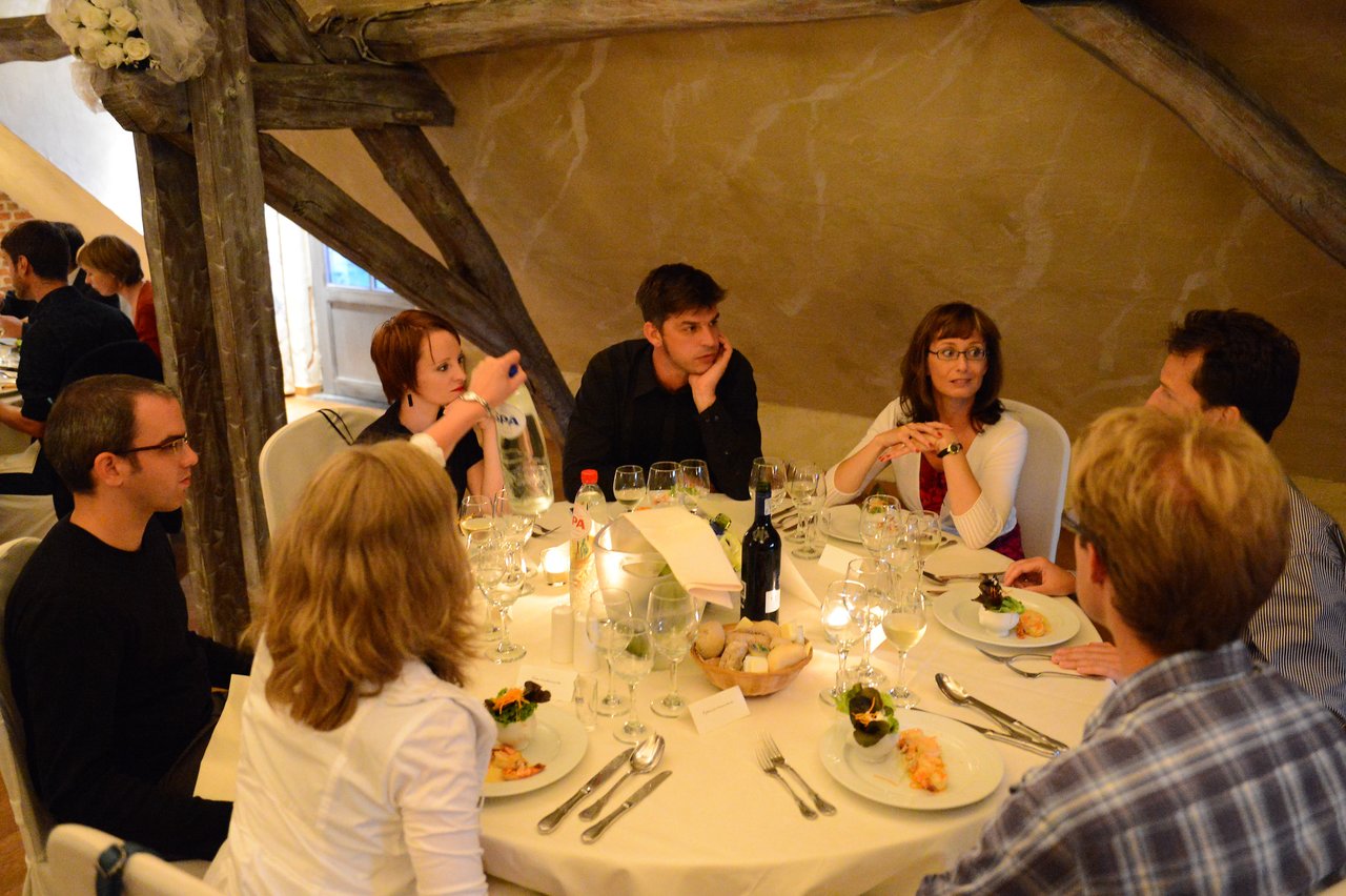 Guests sit around a table at a wedding reception, engaged in conversation while enjoying food and drinks.