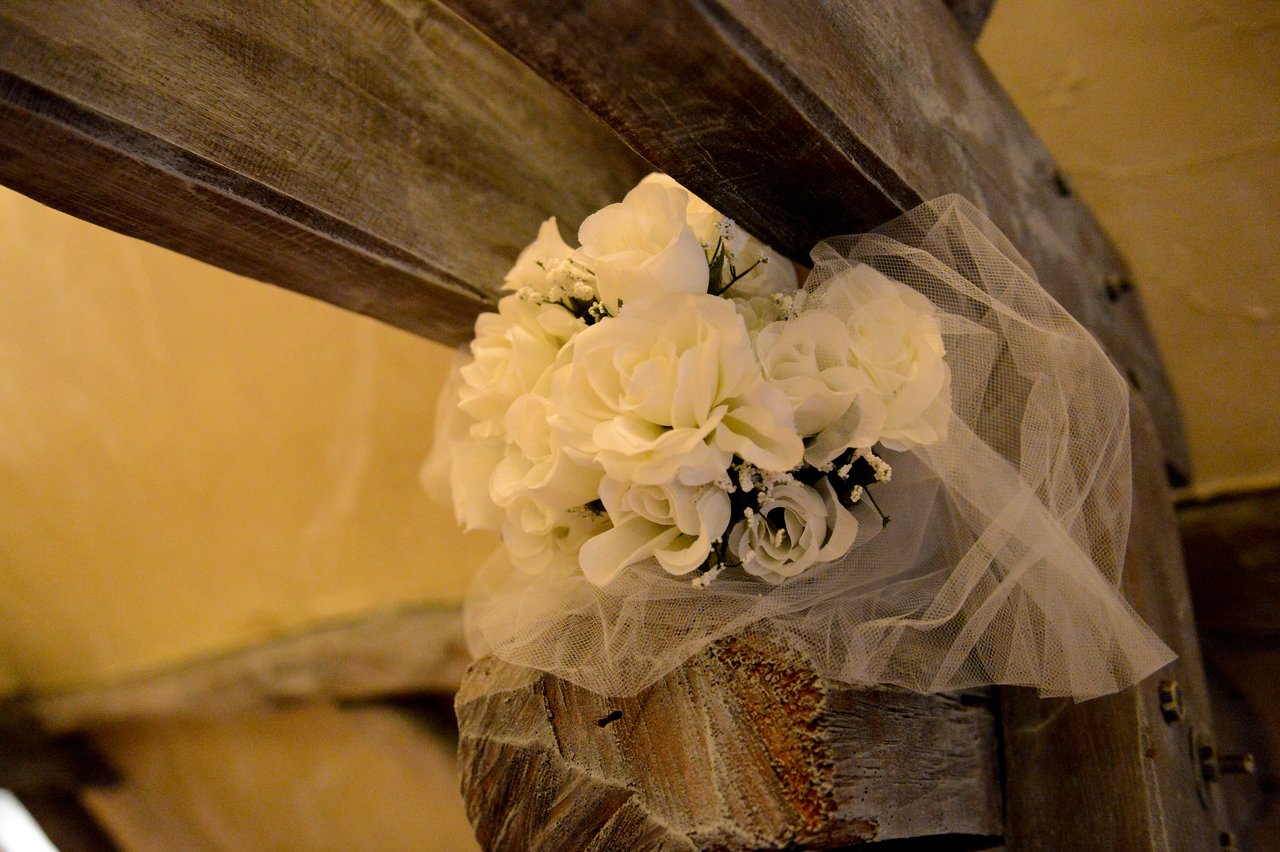 A bouquet of white flowers with tulle is attached to a wooden beam as wedding decoration.