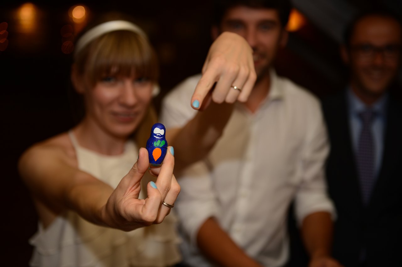 A newlywed couple shows their wedding rings while the bride holds a small painted figurine.