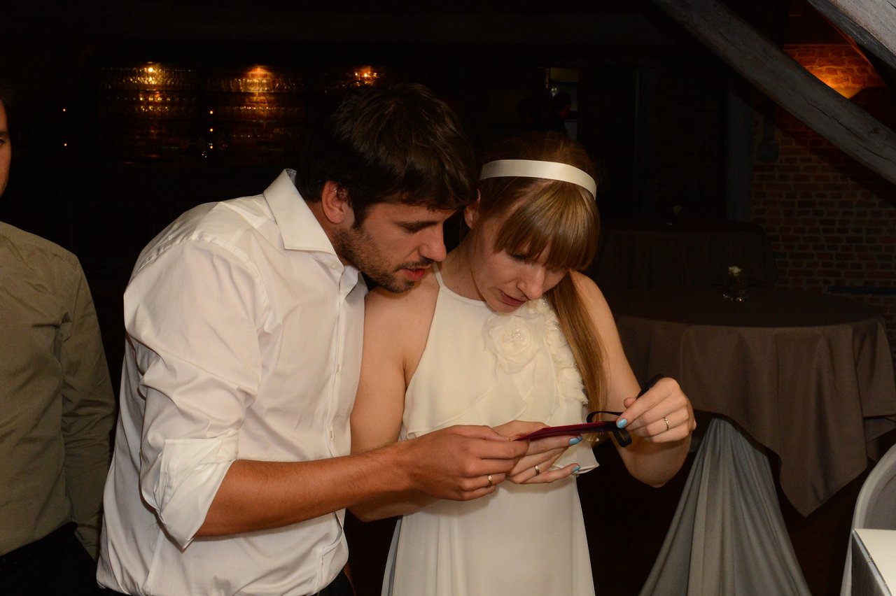 A bride and groom closely examine a small item together at their wedding reception.