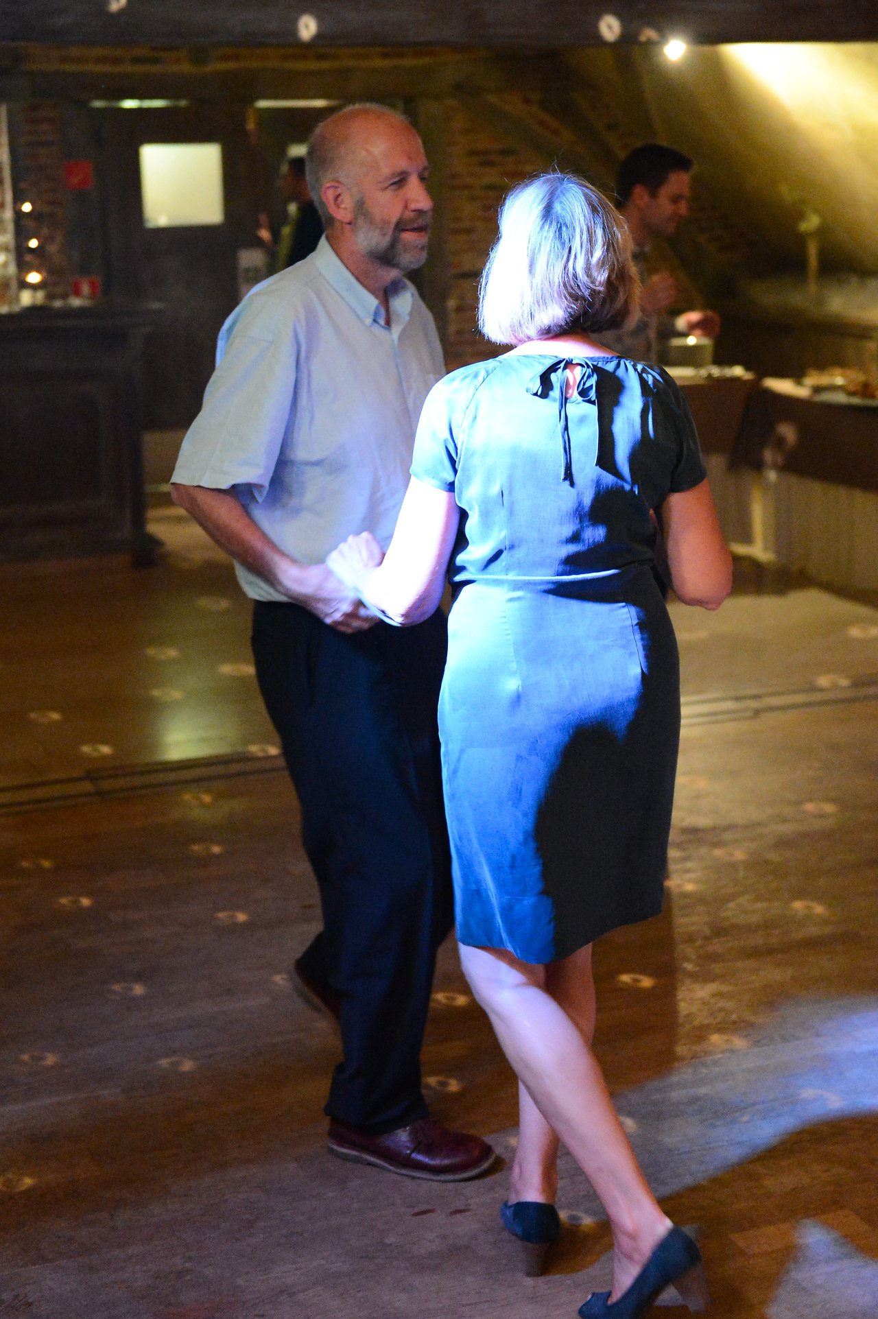 A man and a woman dance together on a wooden floor at a wedding reception.