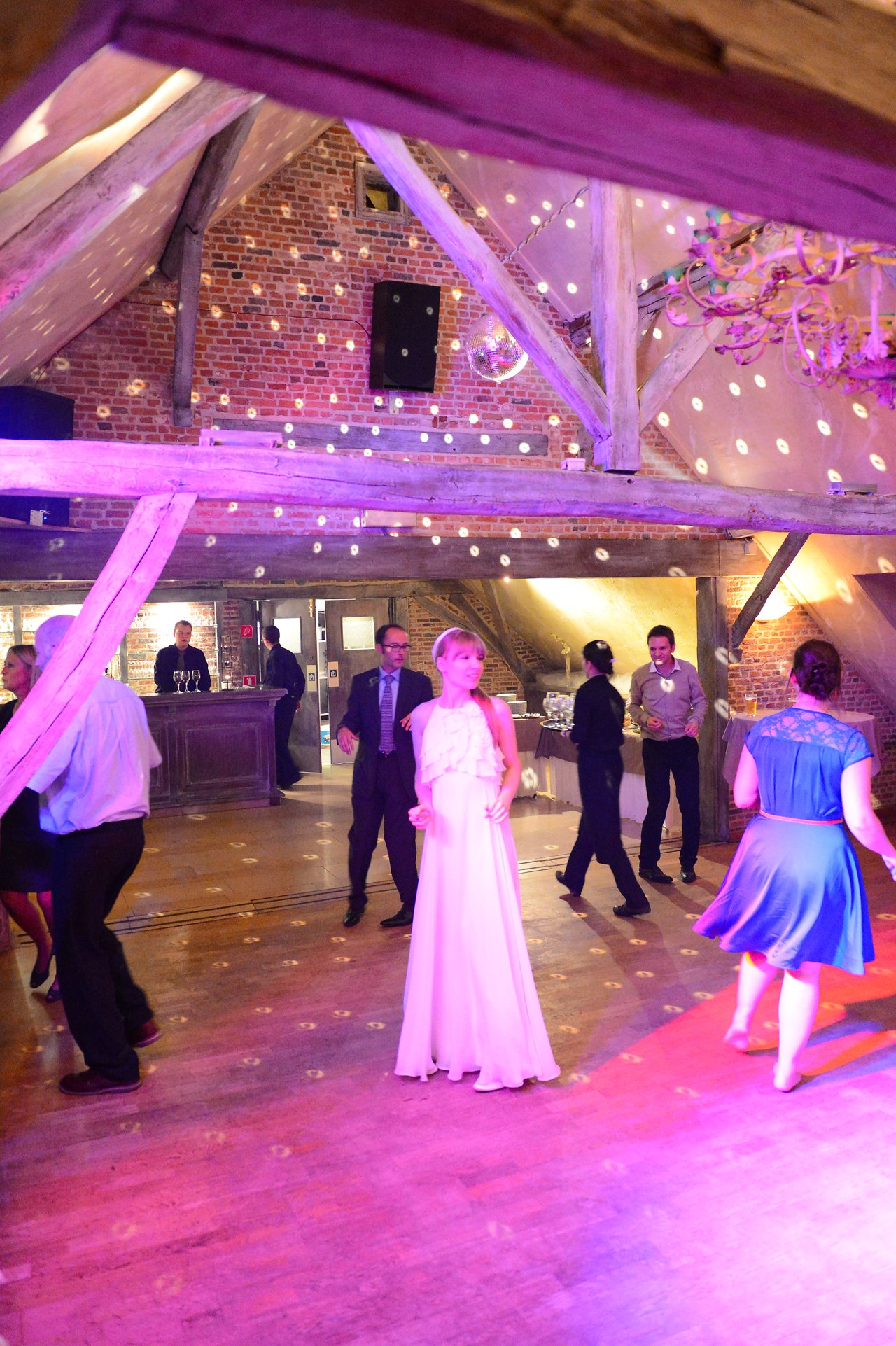 A bride in a white dress stands on the dance floor while guests dance around her at a wedding reception.