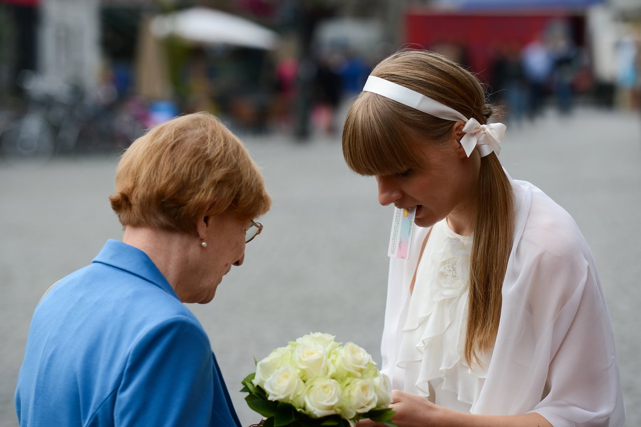 A woman in white hands a bouquet of white roses to an older woman in blue during a wedding.