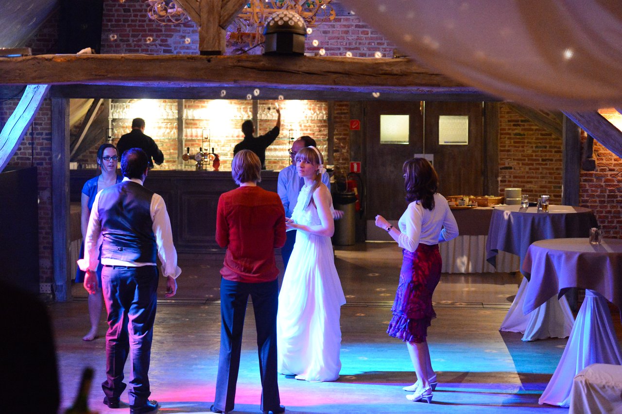 The bride in a white dress stands with a small group of guests, talking and interacting at the wedding reception.