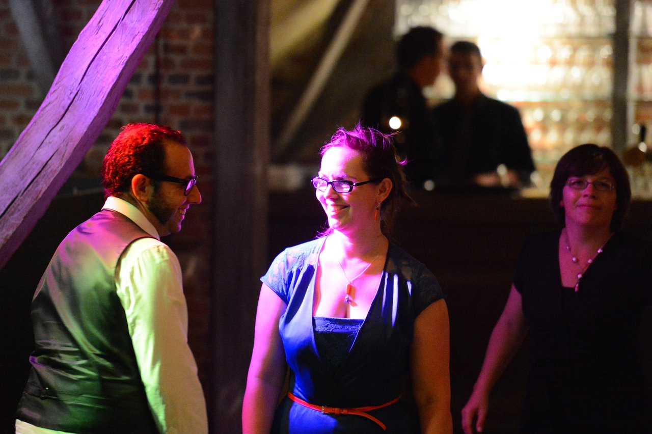 A man and a woman smile at each other while dancing at a wedding reception, with guests in the background.