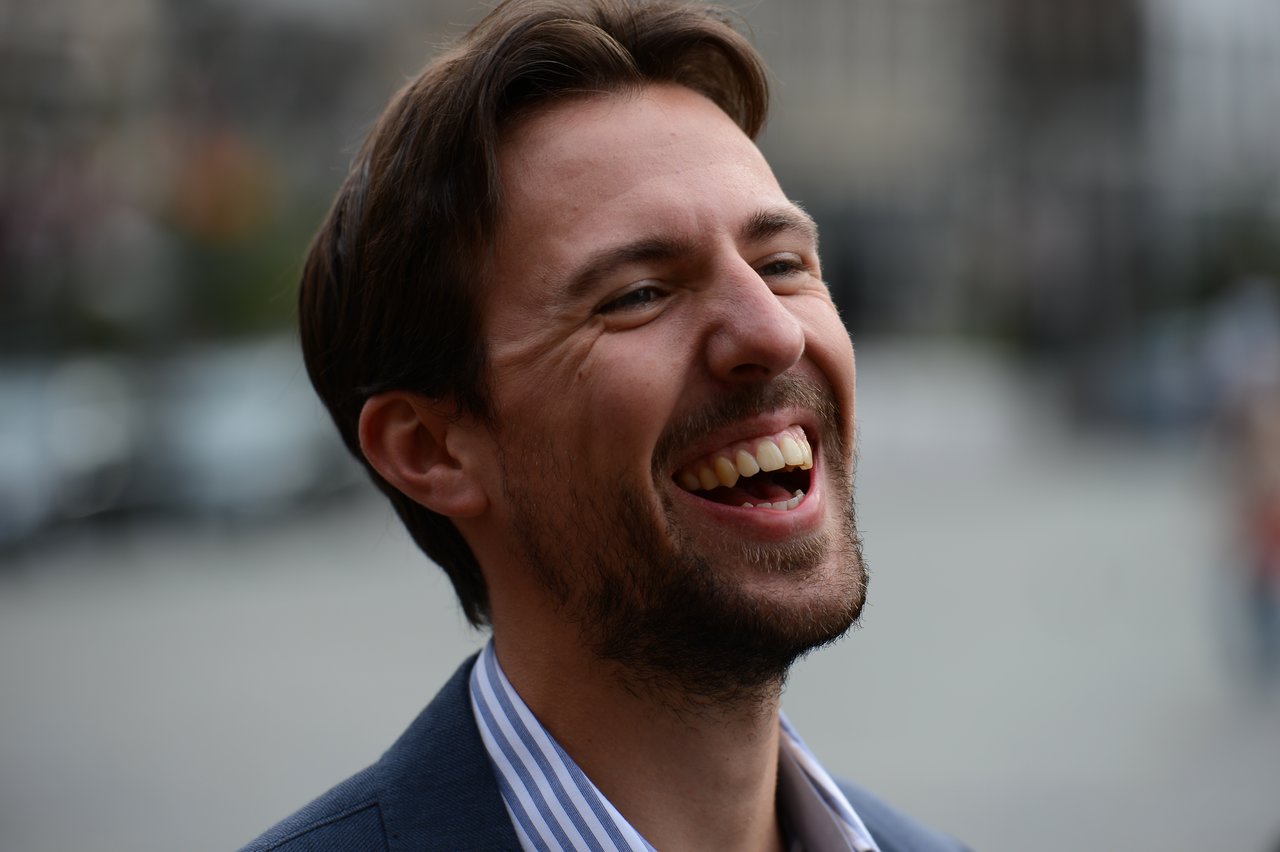 A man in a suit laughing joyfully outdoors.