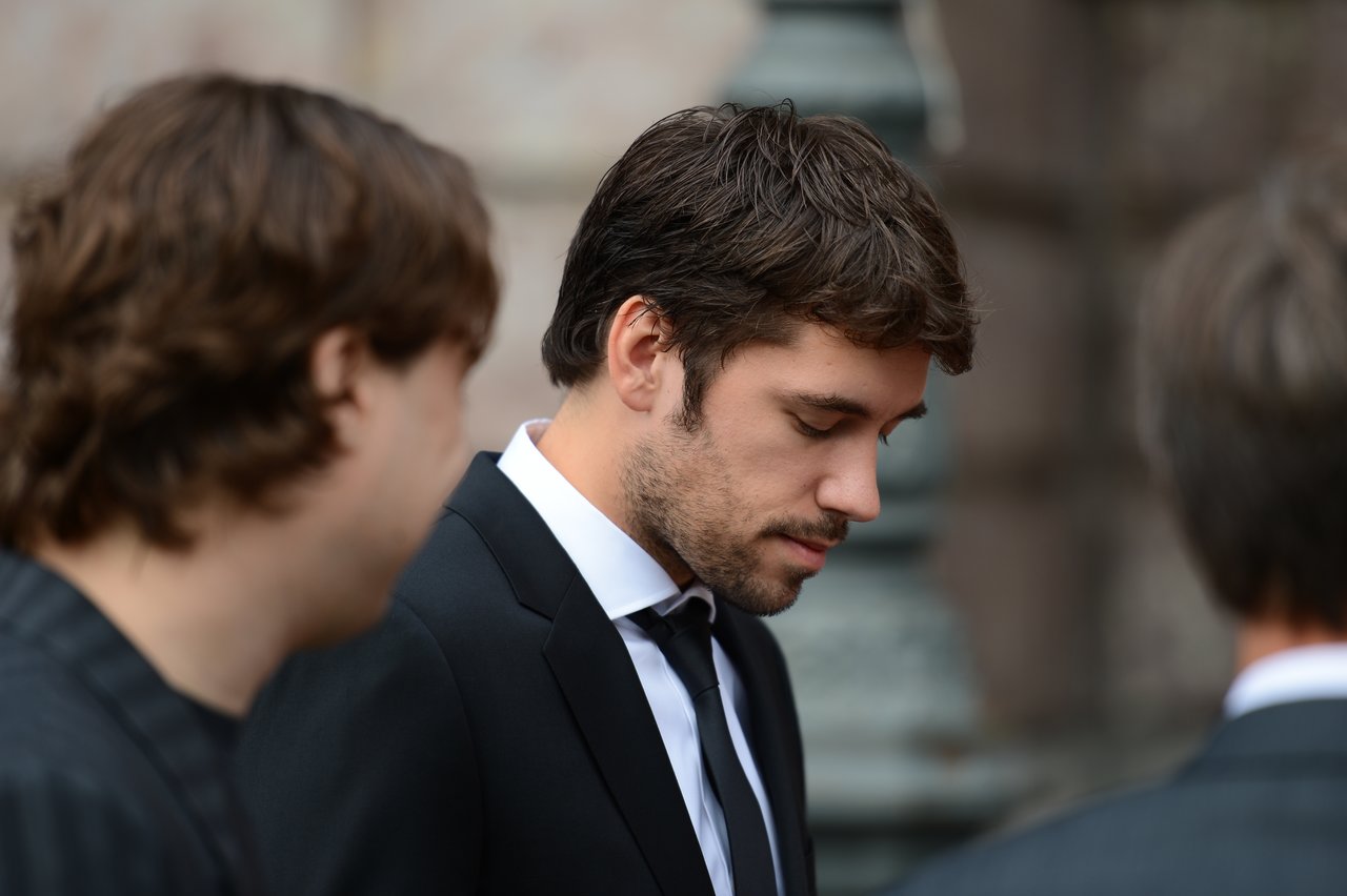 A man in a suit looks down while standing among others at a wedding gathering.