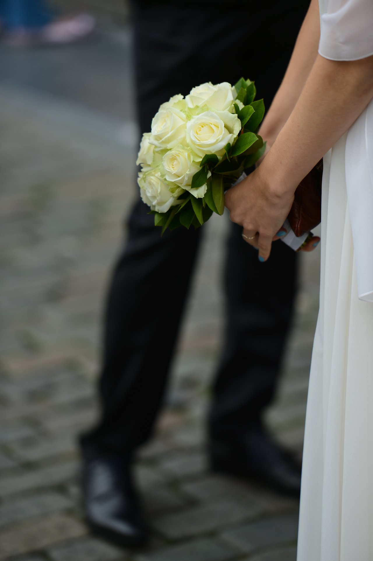 A bride holds a bouquet of white roses while standing next to a groom in formal attire.