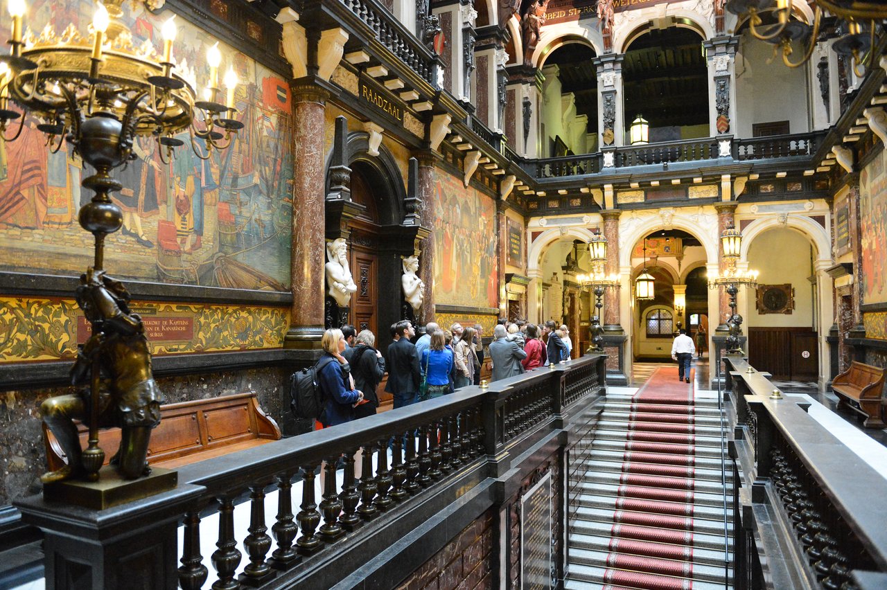 A group of people gathers in an ornate hall, possibly waiting for a wedding ceremony to begin.