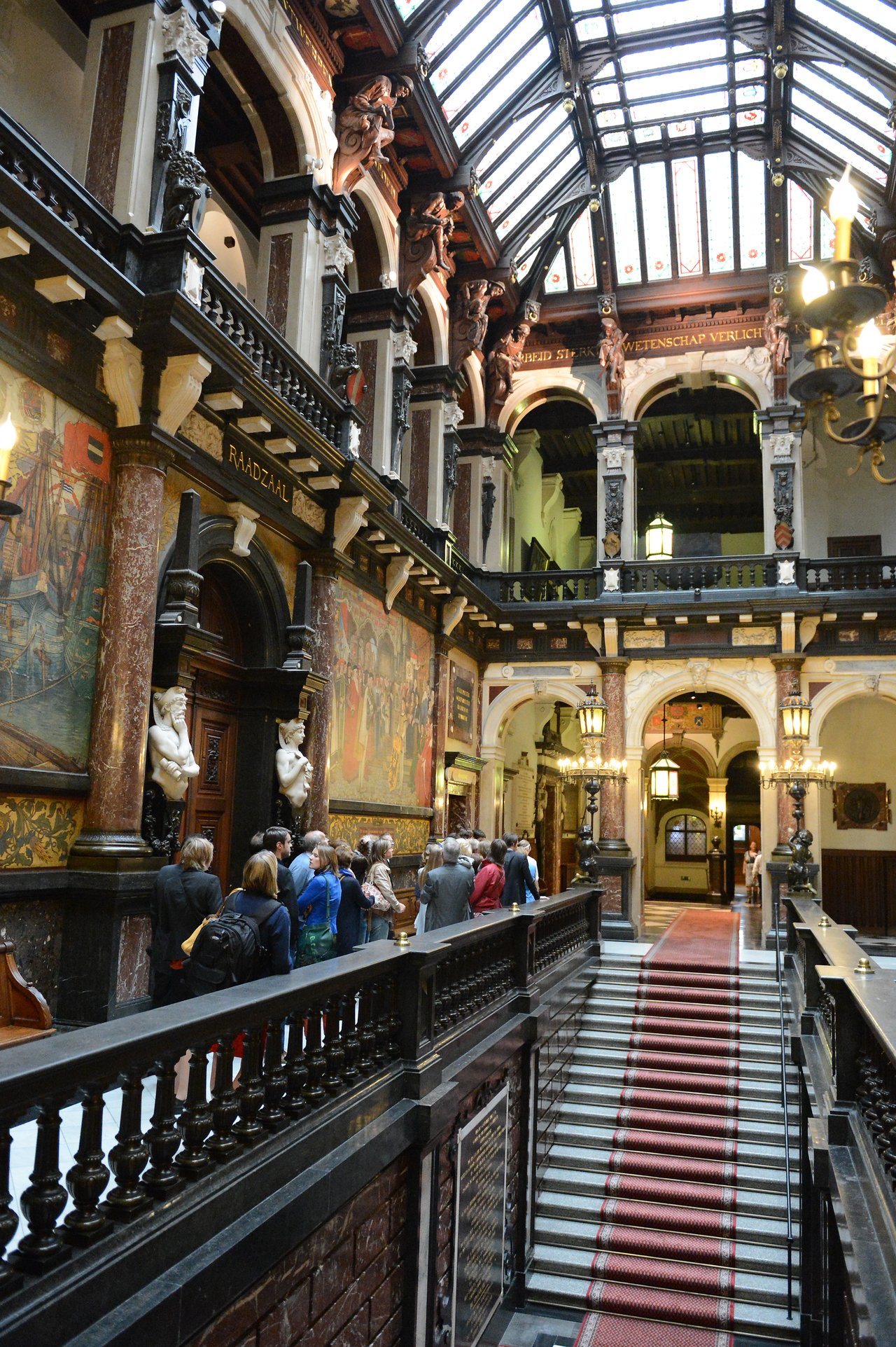 A group of people in formal attire stand in line inside an ornate hall with high ceilings and artwork.