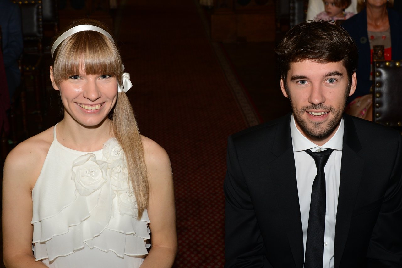 A smiling bride in a white dress and groom in a black suit sit together during their wedding ceremony.