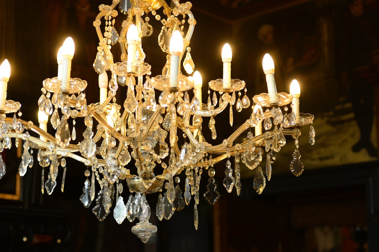 A lit crystal chandelier hanging from the ceiling in a warmly lit wedding venue.
