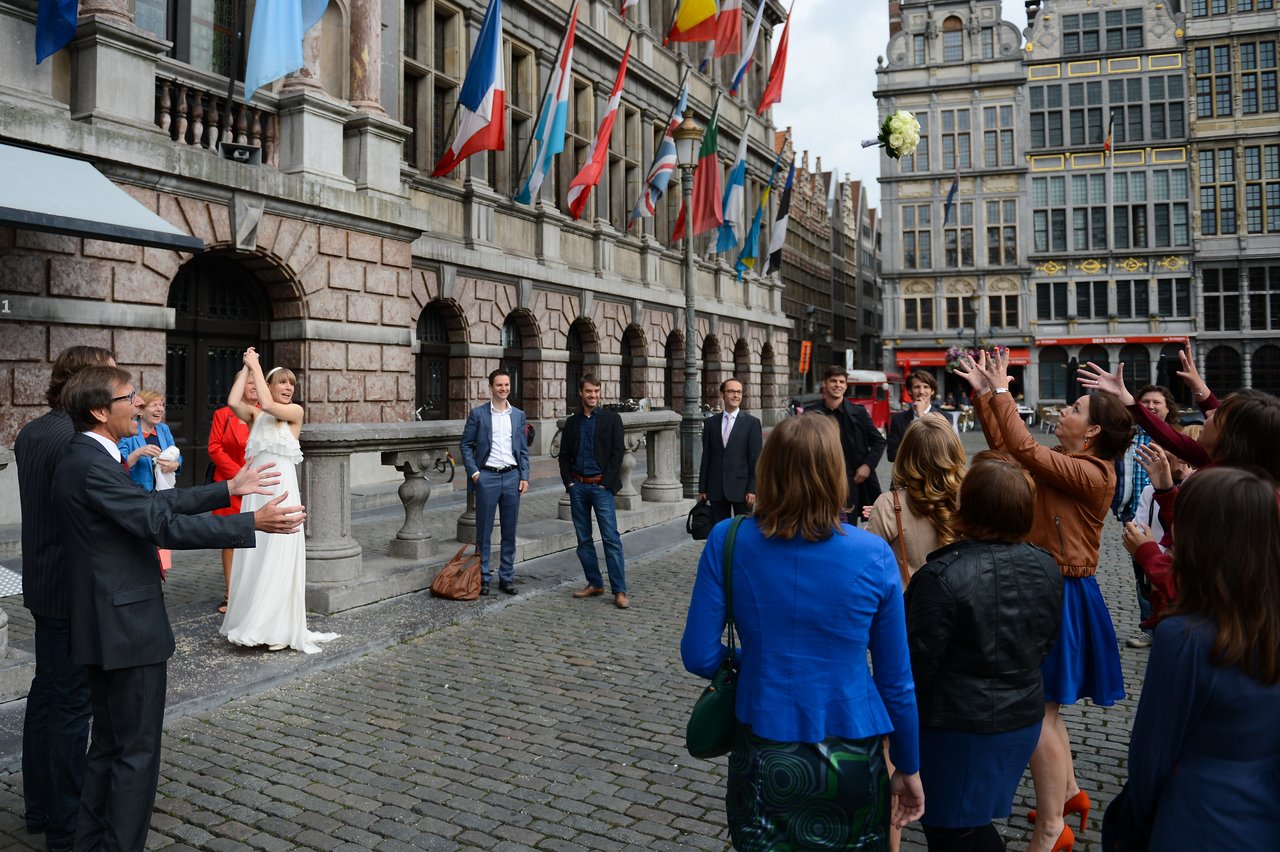 A bride in a white dress throws her bouquet as a group of women reach to catch it.