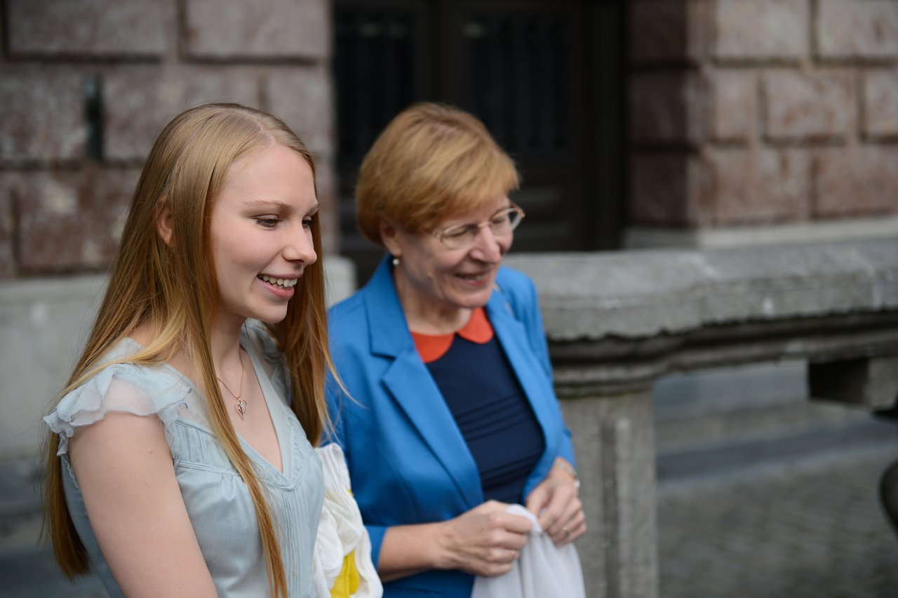 Two women smiling and walking outside during a wedding celebration, holding small fabric bags.