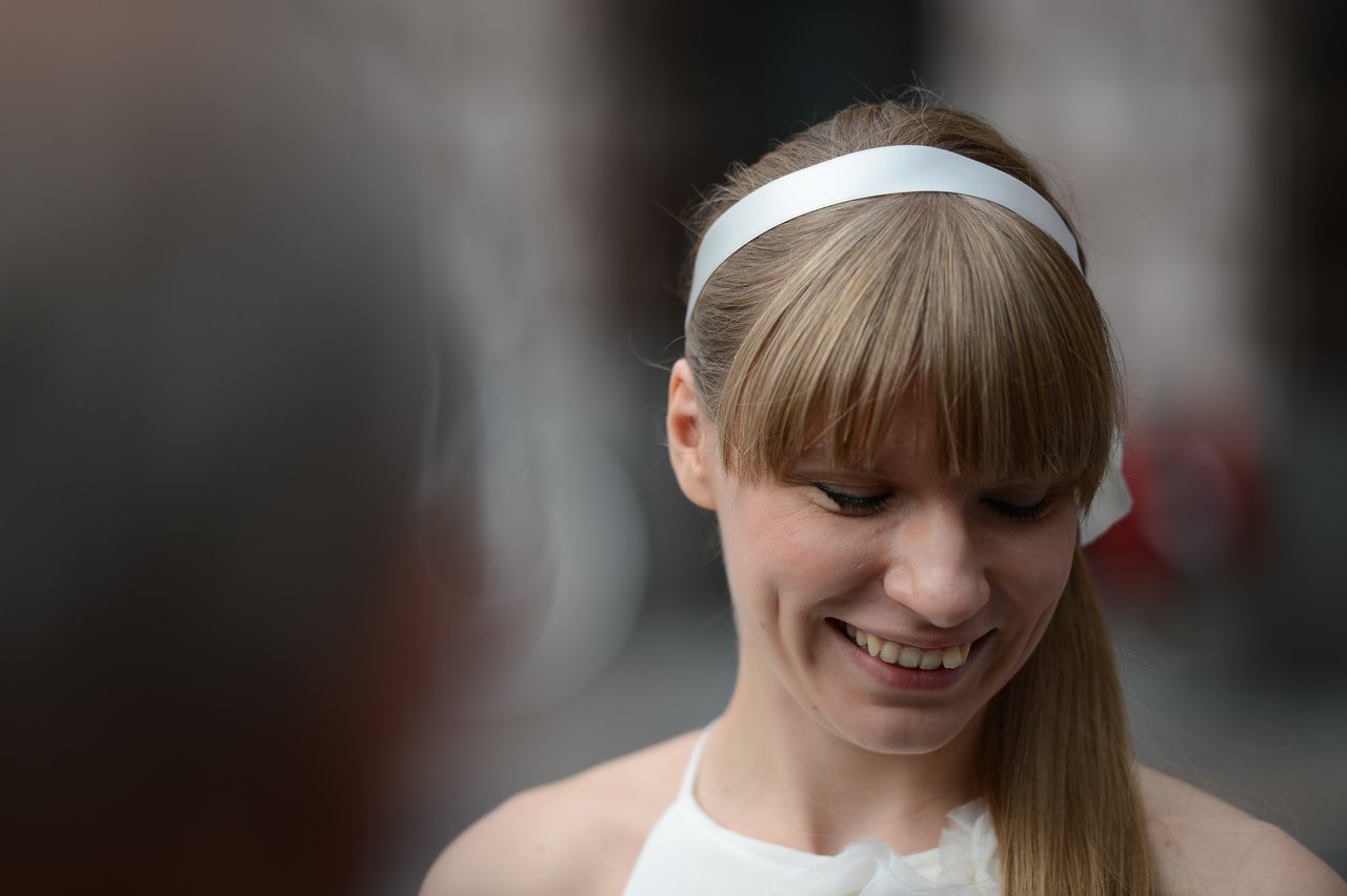 A bride with a white headband smiles while looking down during a wedding celebration.