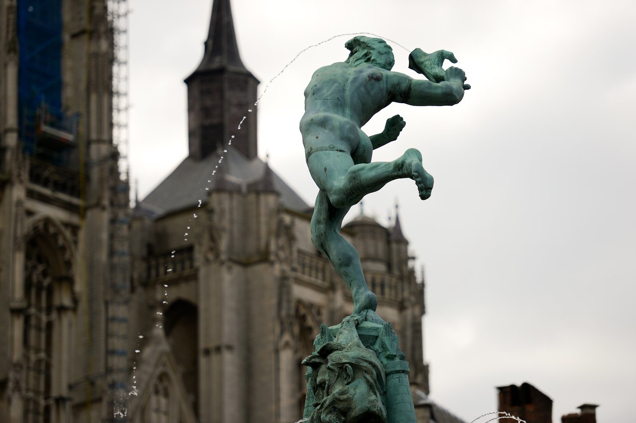A bronze fountain statue of a man mid-leap, with water spraying, in front of a historic church.
