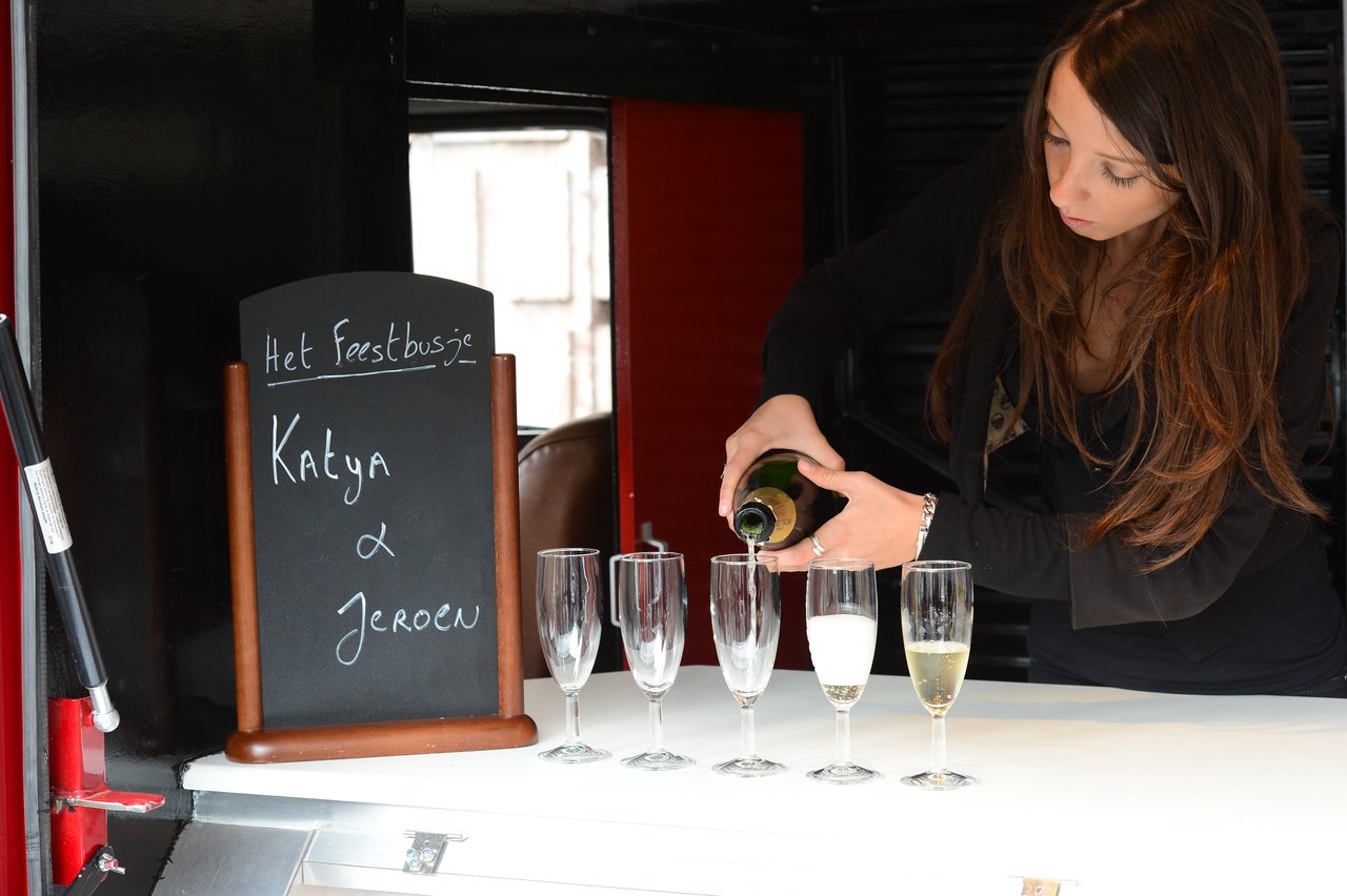 A woman pours champagne into glasses next to a sign with "Katya &amp; Jeroen" written on it.