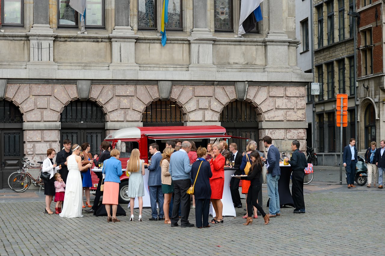 Wedding guests gather outside near a red food truck, chatting and enjoying refreshments.