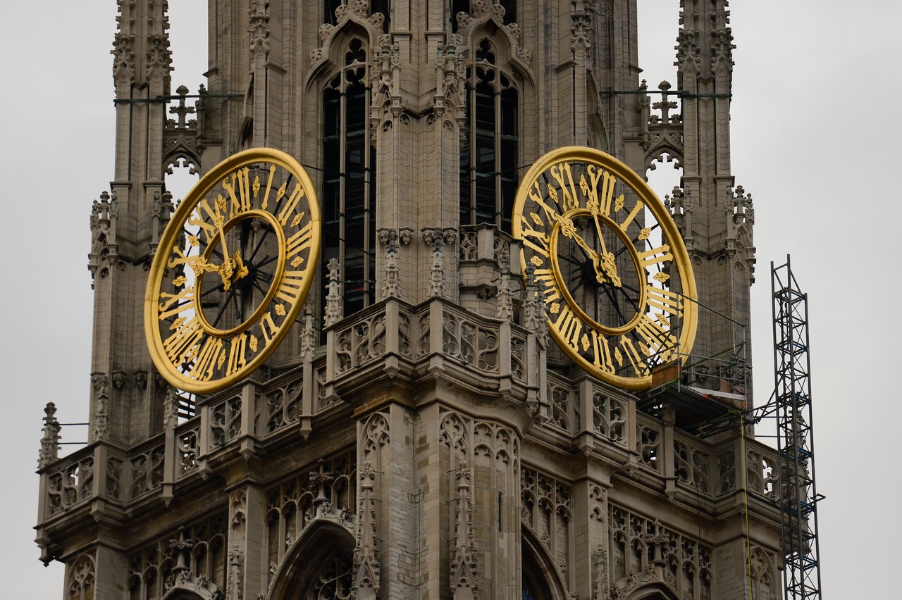 A large church tower with two golden clock faces, one partially disassembled with scaffolding nearby.