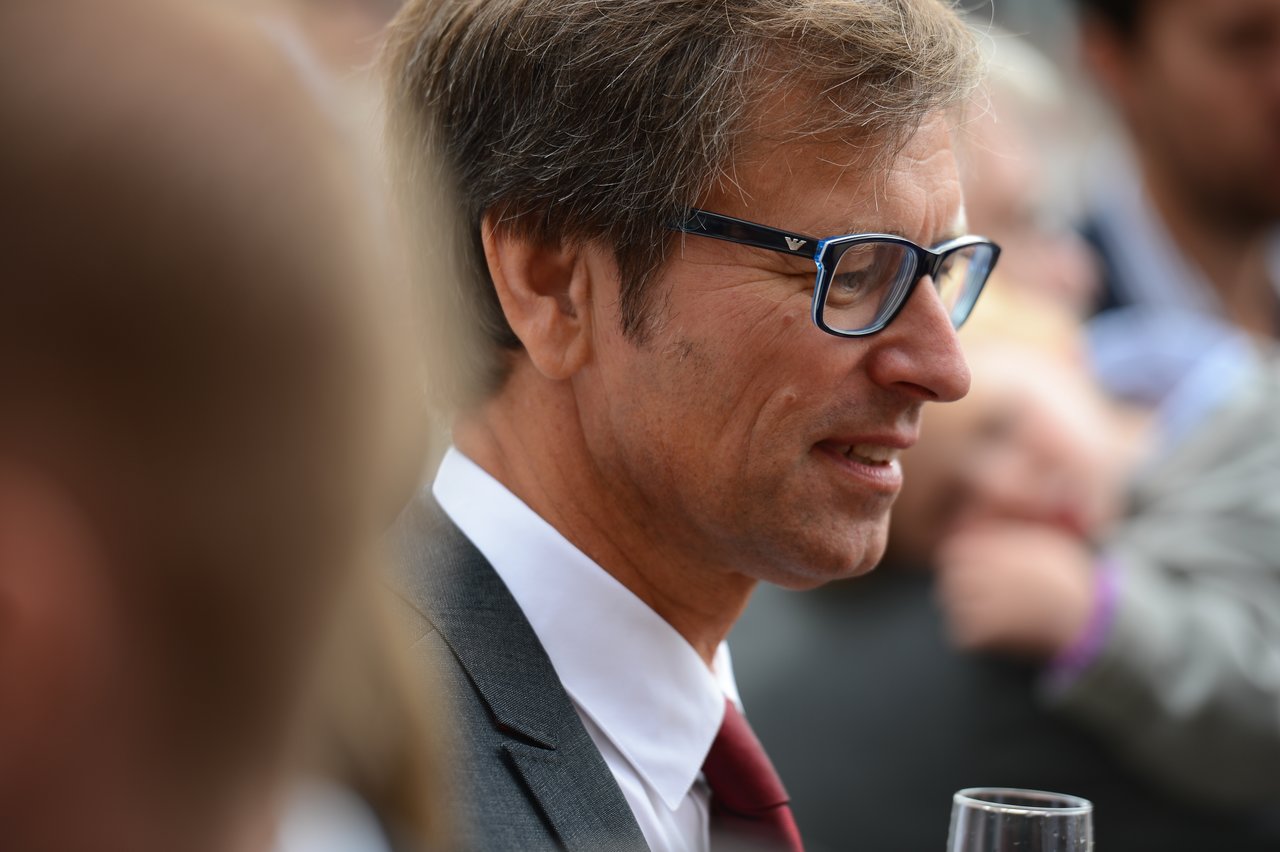 A man in a suit and glasses smiles while holding a glass at a wedding reception.