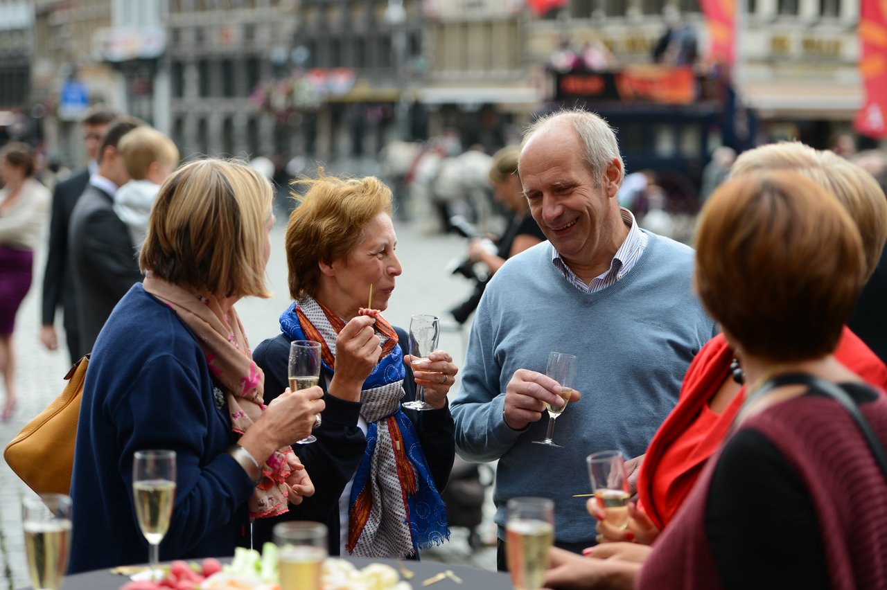 Guests at a wedding reception stand together, chatting and holding glasses of champagne in an outdoor setting.