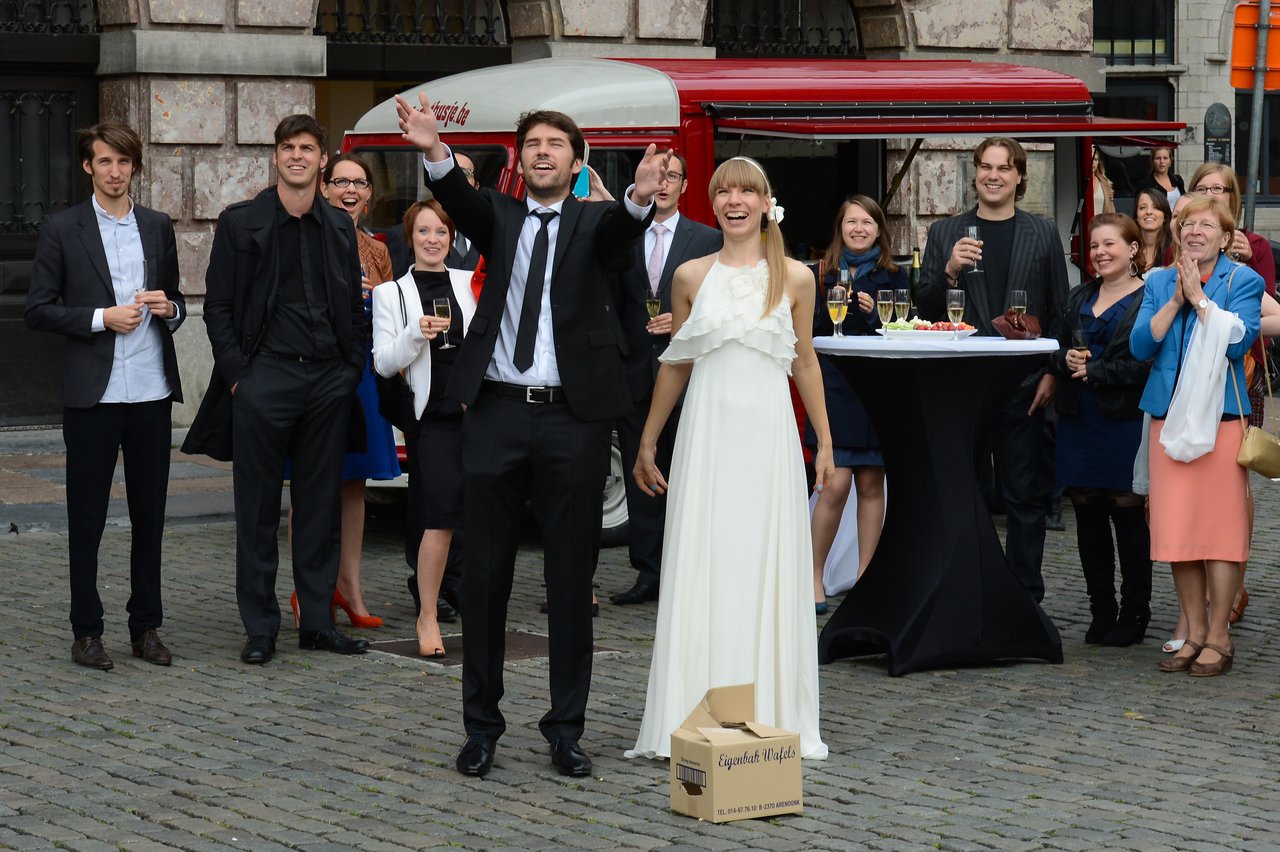 A bride and groom celebrate outdoors with friends and family, smiling and cheering during their wedding reception.