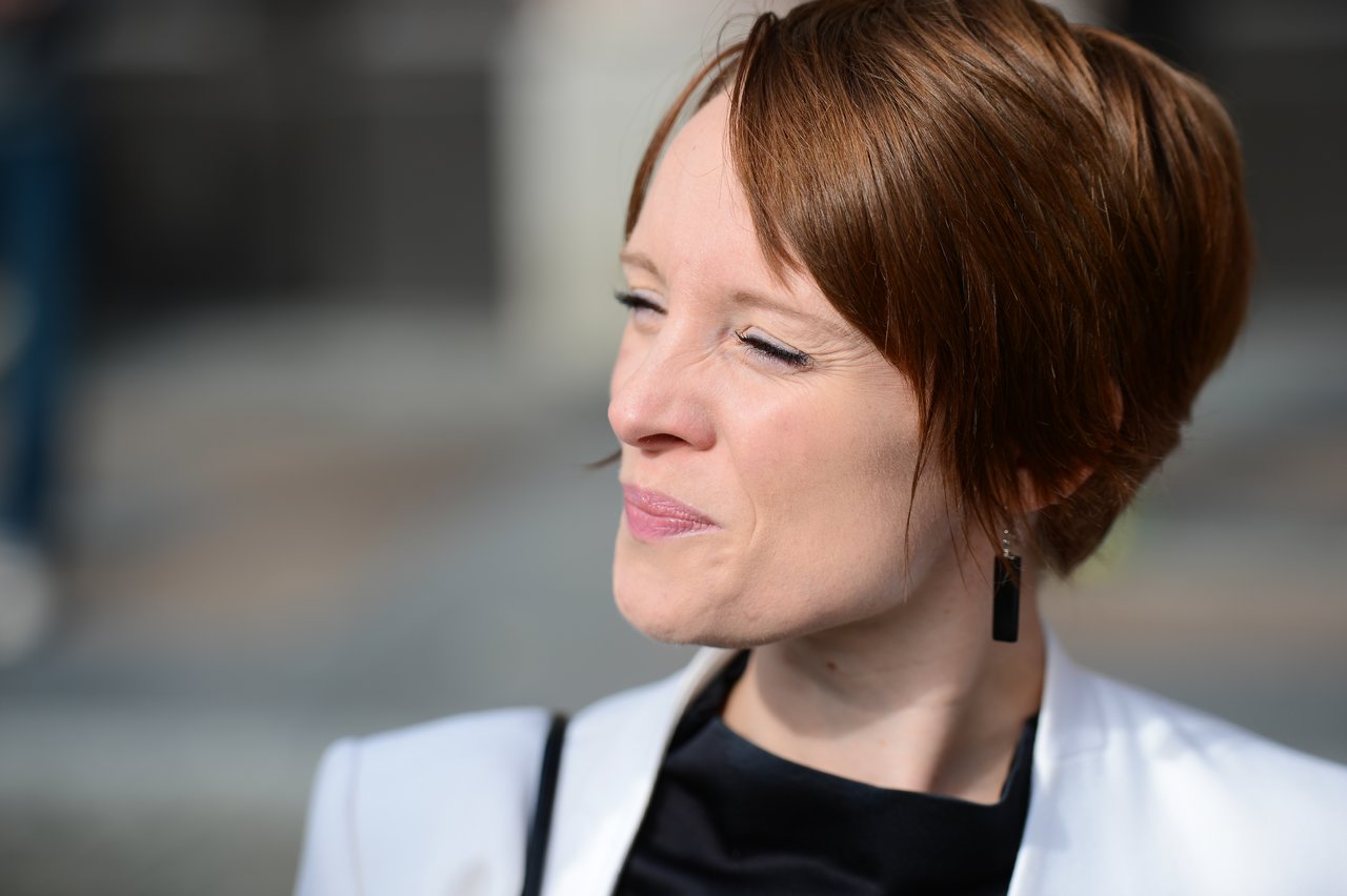 A woman in formal attire squints and smiles in bright sunlight during a wedding celebration.