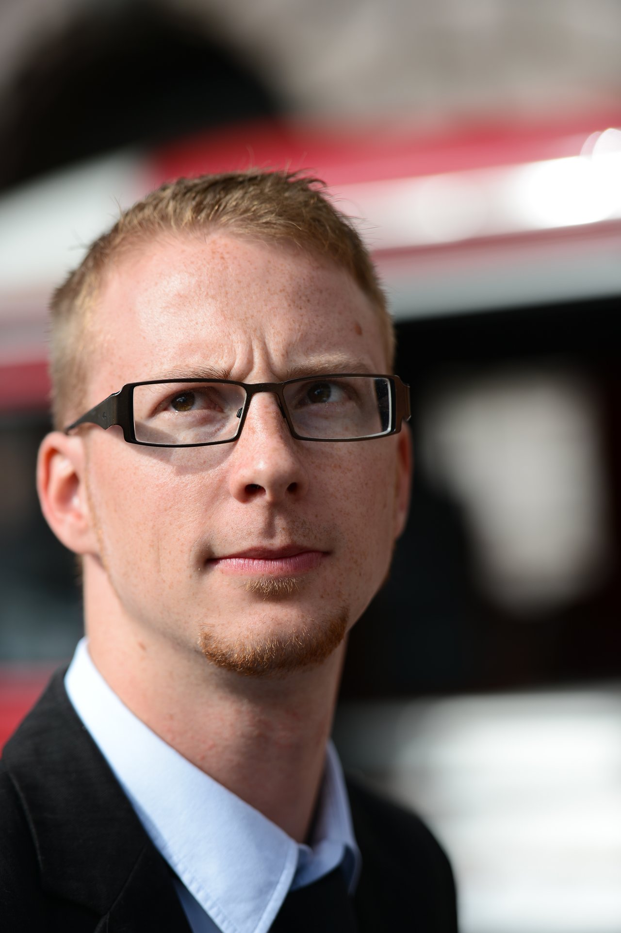A man in formal attire with glasses looks slightly upward, possibly at a wedding event.