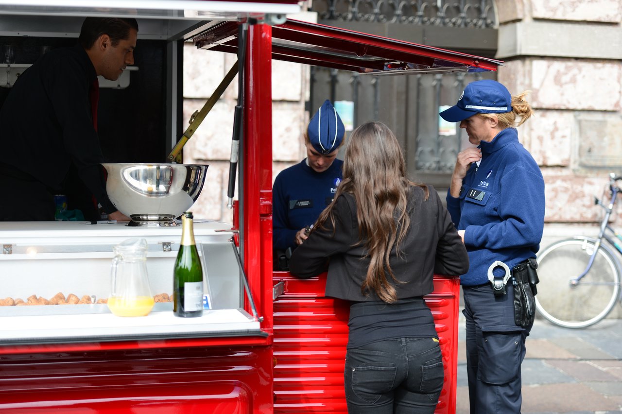 A woman speaks with two police officers at a red food cart while a vendor prepares items inside.