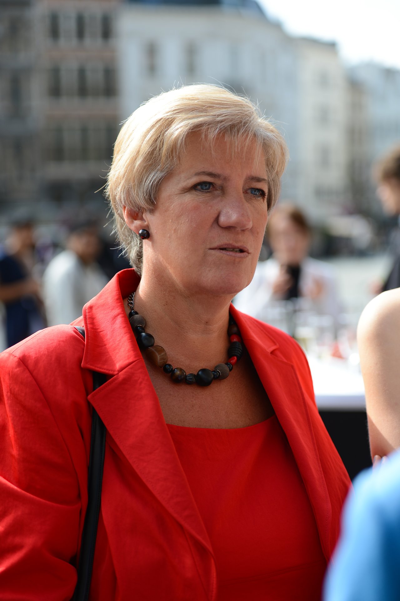 A woman in a red outfit is engaged in conversation at an outdoor wedding reception.