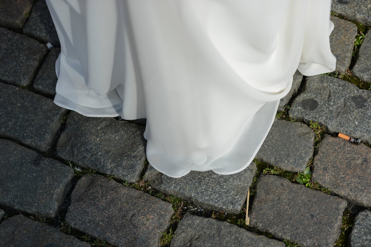 The bottom of a white wedding dress touching a cobblestone ground.