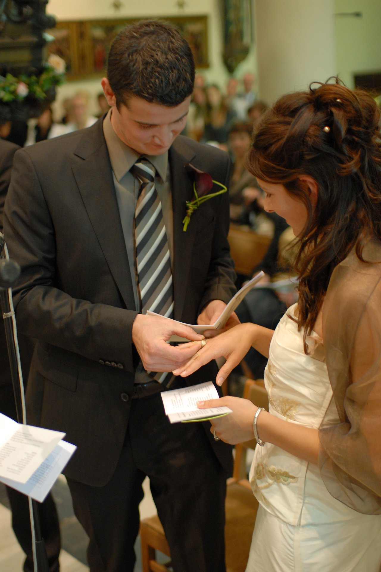 A groom places a wedding ring on the bride's finger during their wedding ceremony in a church.