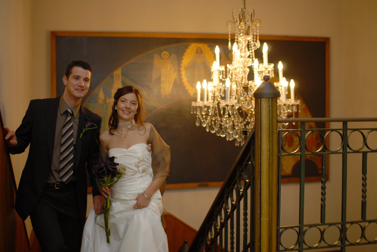 A bride and groom stand on a staircase, smiling.
