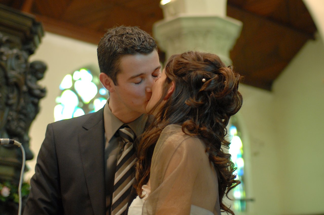 A bride and groom share a kiss during their wedding ceremony inside a church.