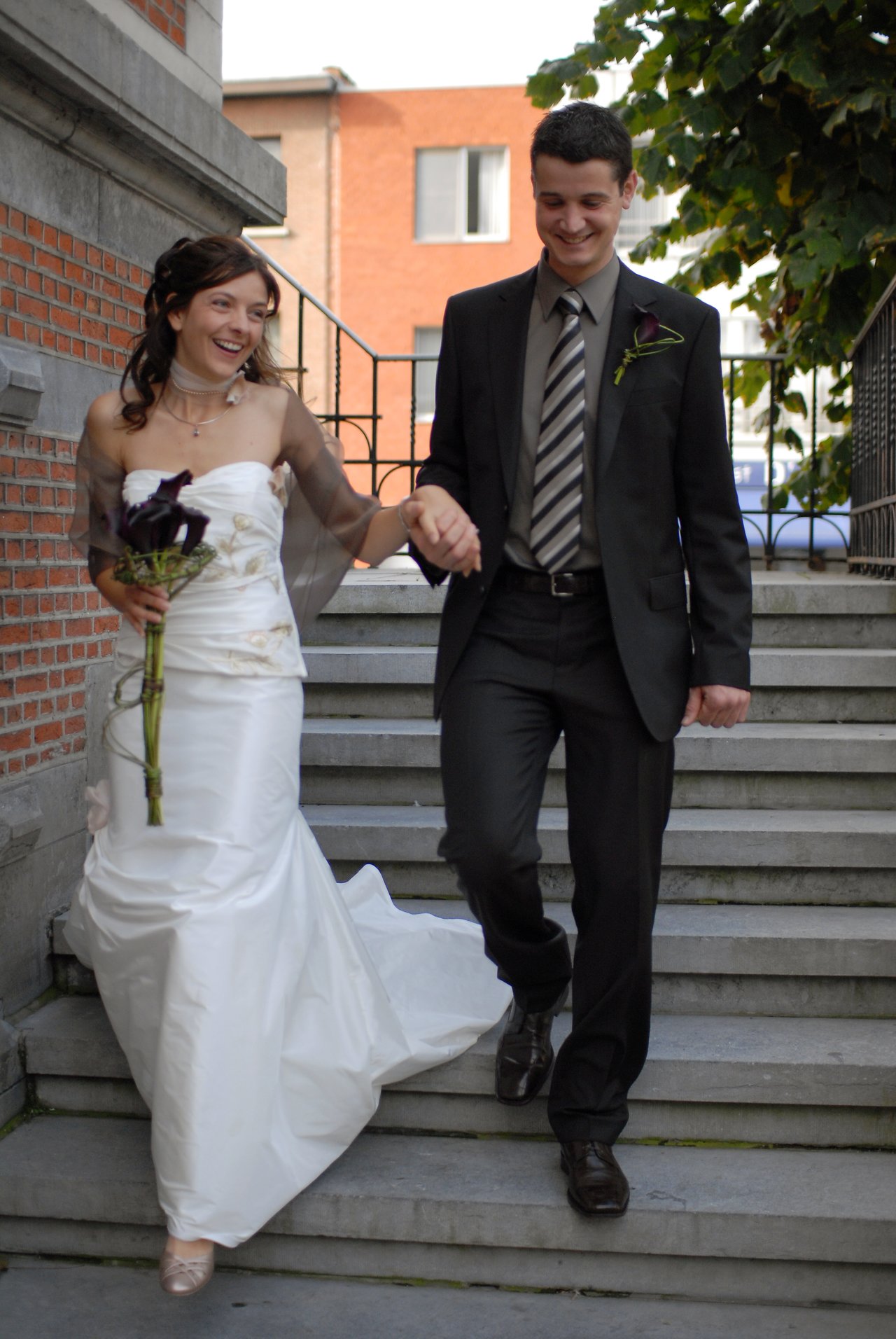 A bride and groom walk down outdoor steps, holding hands and smiling.