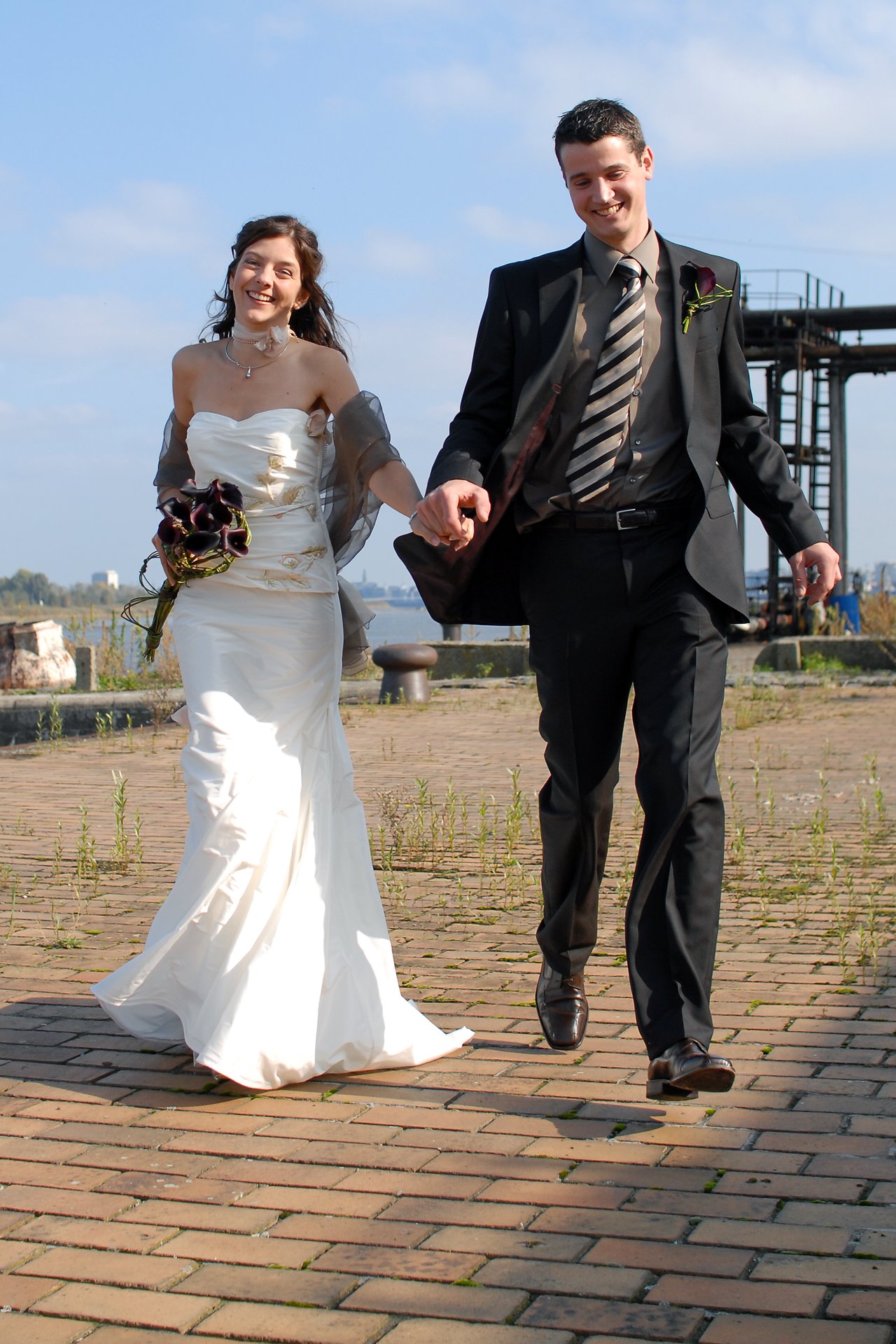 A bride and groom walk hand in hand outdoors, smiling.