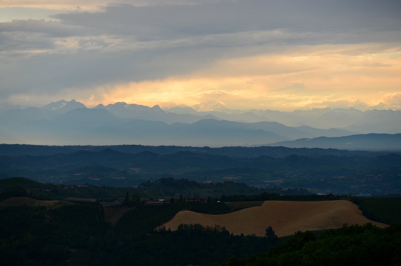 A scenic view of rolling hills and distant mountains under a cloudy sky with warm light at the horizon.