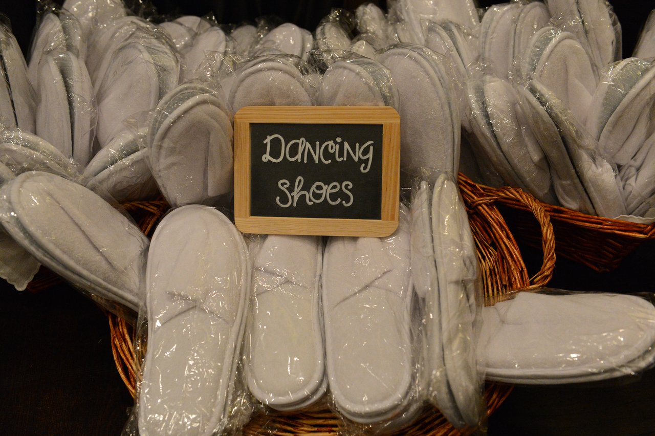 Baskets filled with white slippers labeled "Dancing Shoes" for wedding guests.