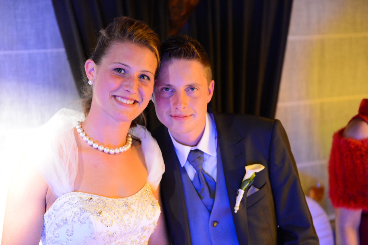 A bride and groom smile while posing together at their wedding reception.