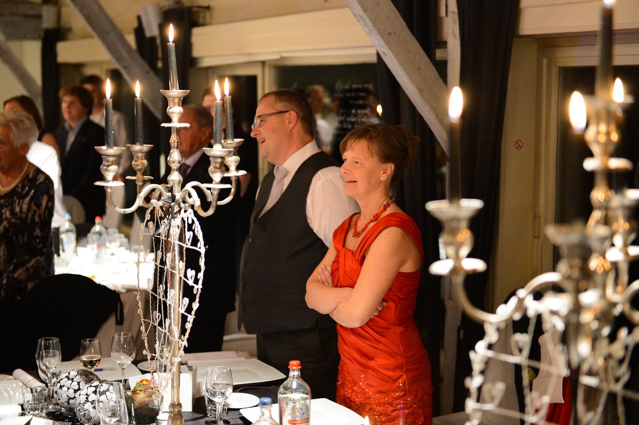 Guests in formal attire stand and smile at a wedding reception, surrounded by candlelit decorations and elegantly set tables.