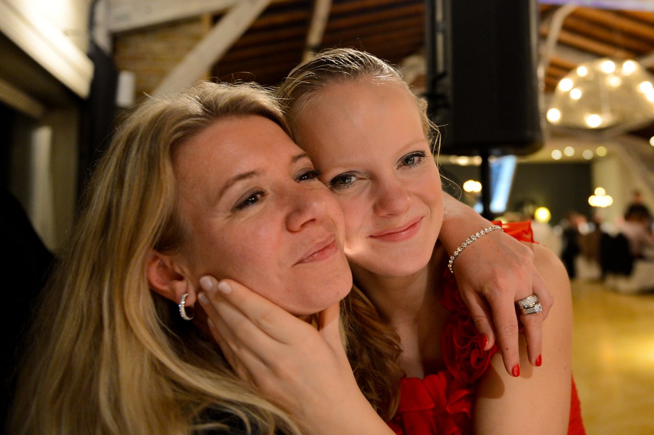 Two women embrace and smile at a wedding reception, with one gently holding the other's face.