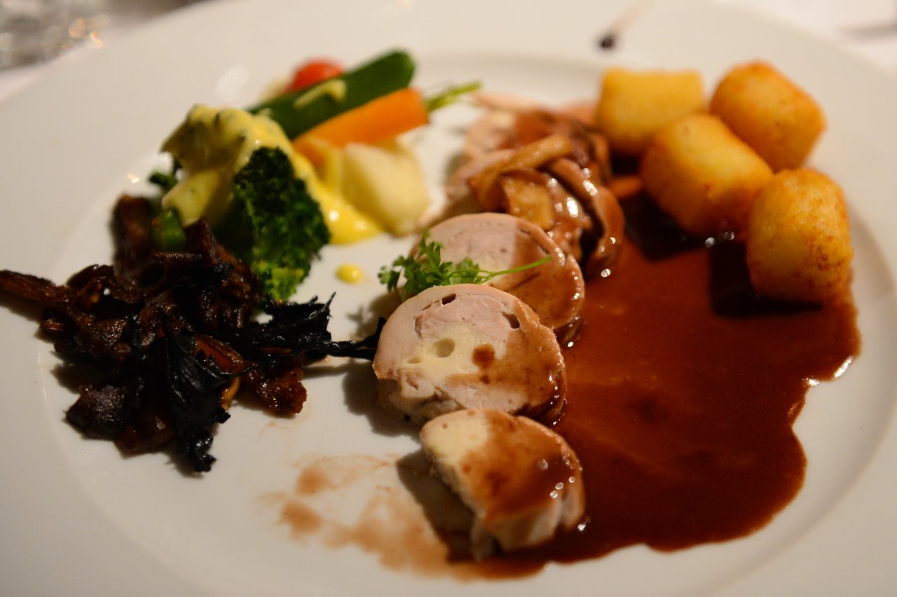 A plated wedding meal with sliced meat in sauce, crispy potatoes, vegetables, and mushrooms on a white dish.