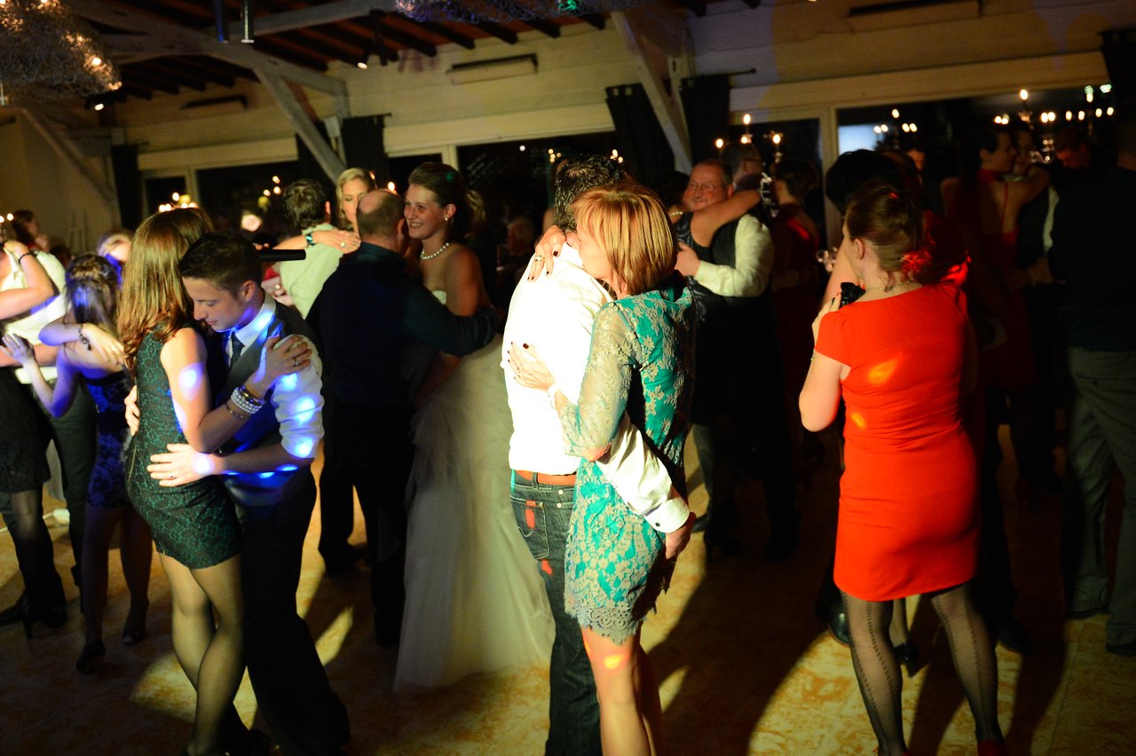 People dancing closely at a wedding reception, with the bride in a white dress among the guests.