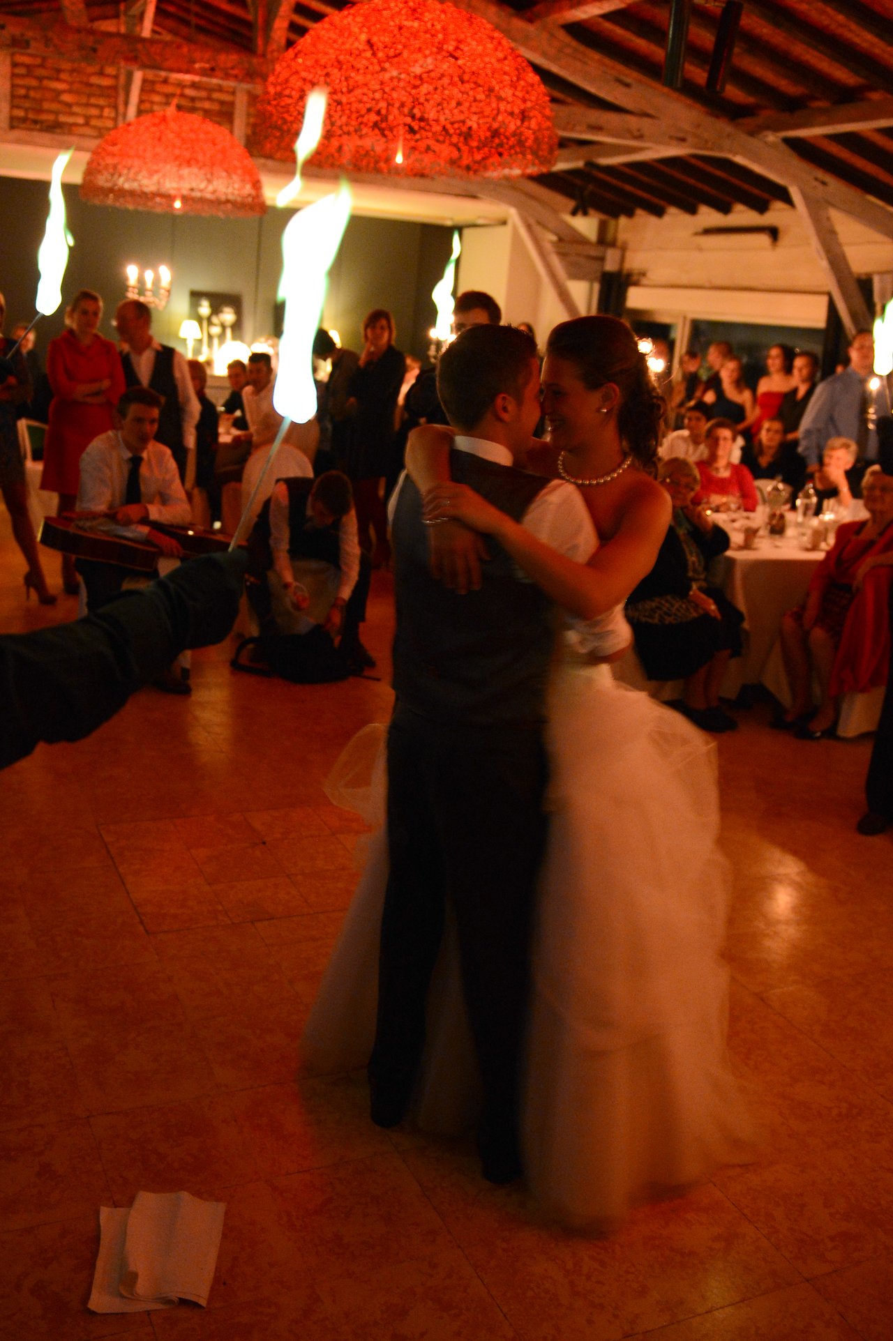 The bride and groom share their first dance while guests watch, with fire performers adding to the celebration.